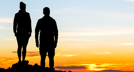 silhouette of man and woman on mountain looking at a sunset
